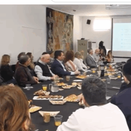 Imagen tomada del canal de YouTube de AMIA. SE ven varias personas sentadas alrededor de una mesa y una pantalla en uno de los extremos